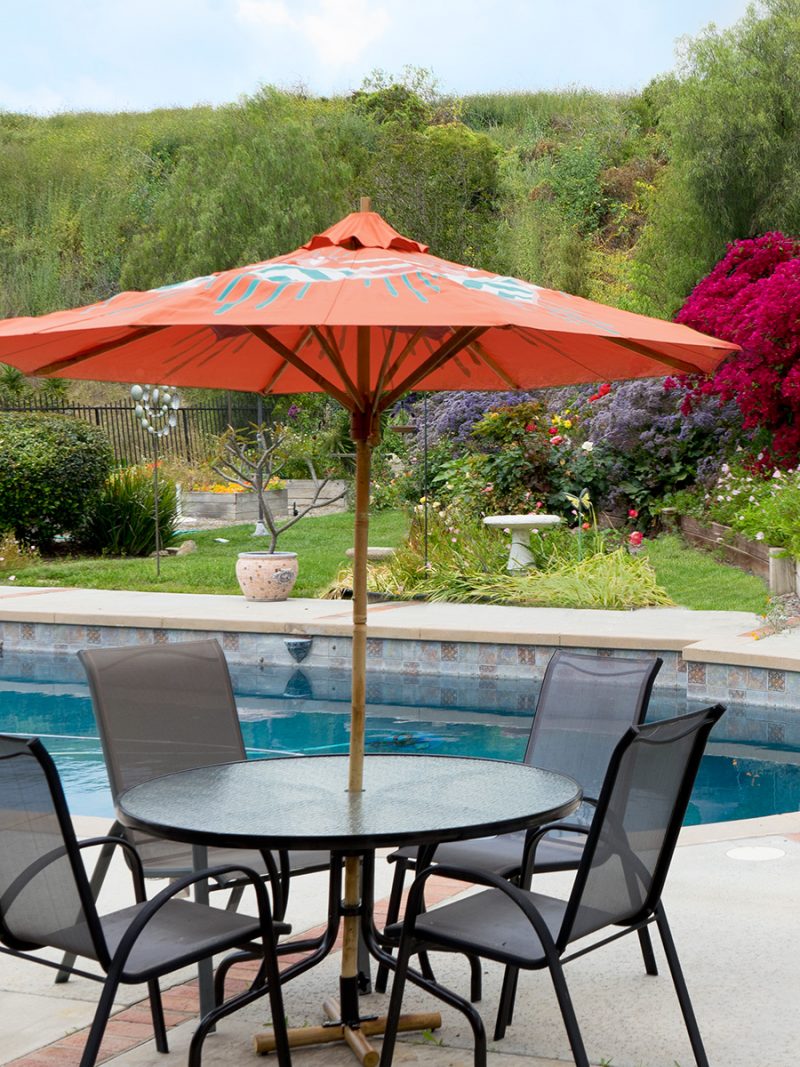 colorful custom patio umbrella painted by Teale Hatheway of pearl and maude - beautiful poolside space with orange umbrella