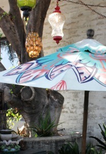 turquoise and coral hand painted patio umbrella in the garden with trees and hanging lanterns